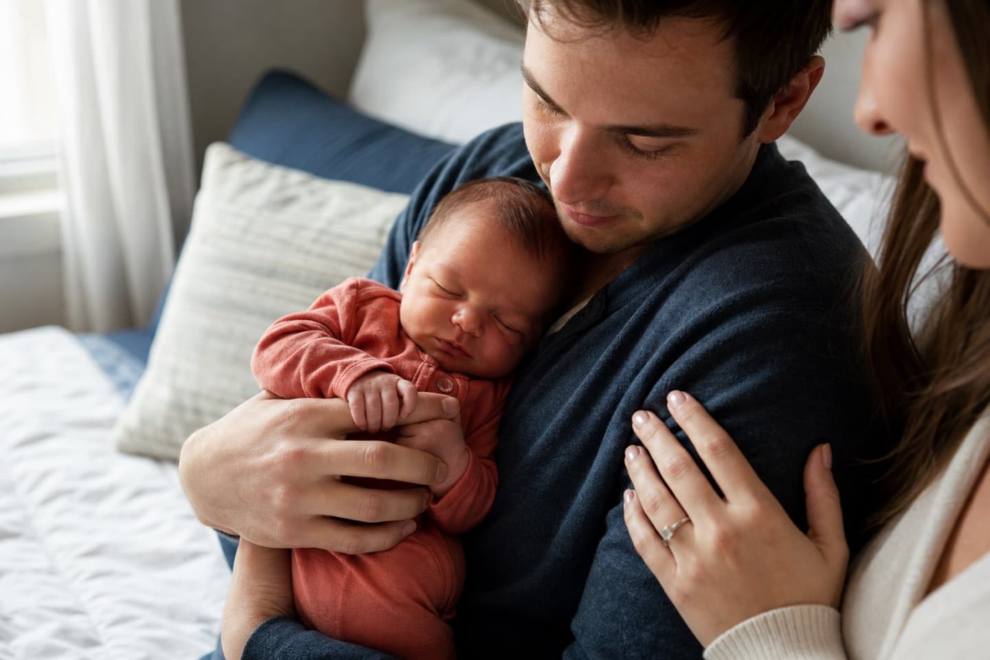 A safely held newborn gripping a parent's finger during a quiet family moment